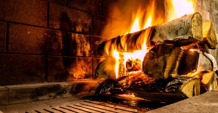 Flames flicker in a fireplace, with logs burning and glowing embers visible on a metal grate.