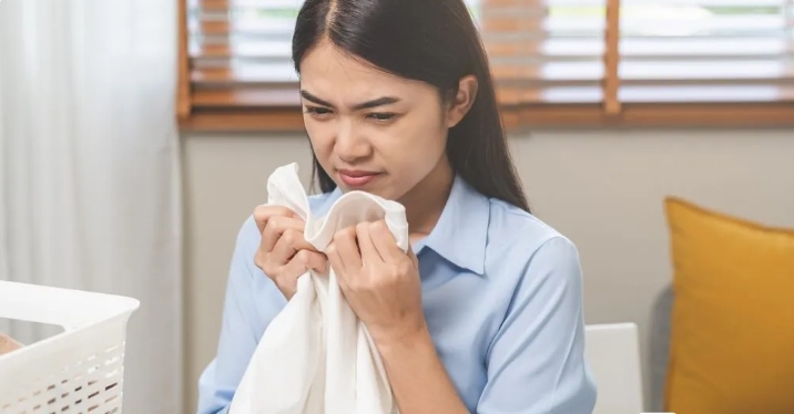 A woman frowns while holding a damp cloth, indicating concern over musty odors.