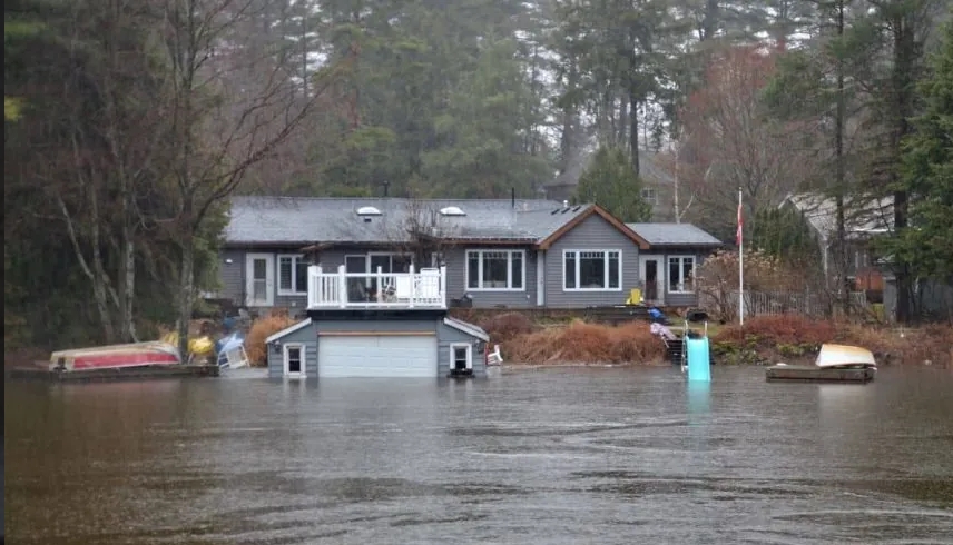 A house partially submerged in floodwaters, surrounded by trees and debris, illustrating spring flooding risks.