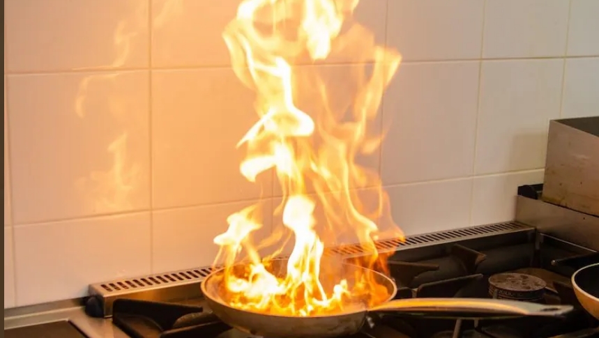 Flames erupt from a frying pan on a stove, highlighting the risk of kitchen fires.