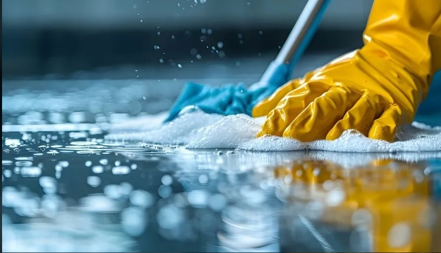 Hands in yellow gloves cleaning a wet surface with a mop, surrounded by bubbles and water droplets.