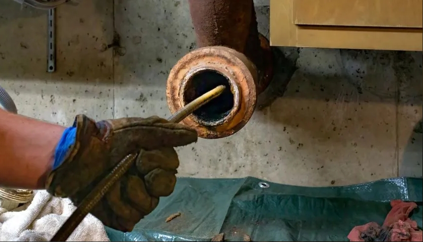 A gloved hand uses a tool to inspect a sewer pipe in a home setting, addressing sewer gas issues.