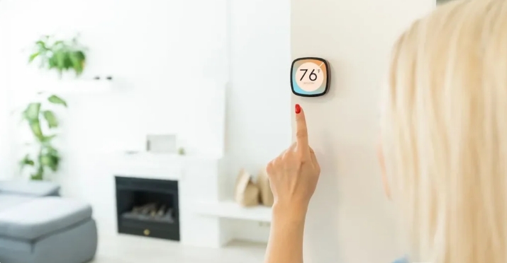 A person adjusts a smart thermostat displaying a temperature of 76°F in a modern living room.