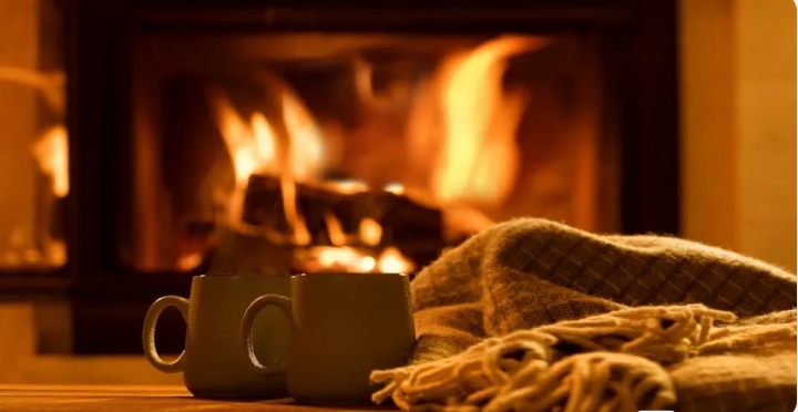 Warm fireplace with glowing flames, two mugs, and a cozy blanket in the foreground.