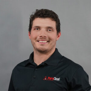 A smiling man in a black PuroClean polo shirt poses against a gray background.
