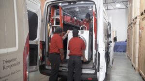 Workers loading a washing machine into a water mitigation van, with