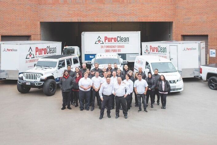 The PuroClean team stands proudly with their branded emergency service vehicles and trailers.
