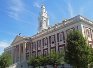 A classical red brick building with white columns, an American flag, and a tall clock tower under