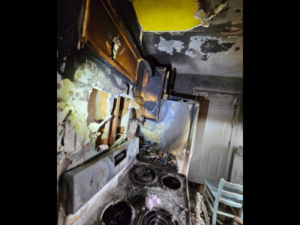 Severe fire and smoke damage in a residential kitchen showing charred cabinets, soot-covered walls, and burnt stovetop appliances.