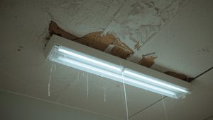 Water dripping from a ceiling light fixture beneath a peeling, water-damaged ceiling