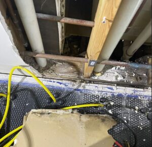 Exposed plumbing pipe behind damaged drywall during a water damage restoration project.