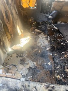 Residential fire mitigation is shown in a heavily destroyed garage structure with collapsed walls, exposed framing, and extensive fire-related debris scattered across the ground. The interior is charred and filled with burned materials, highlighting severe structural loss and smoke damage throughout the building.