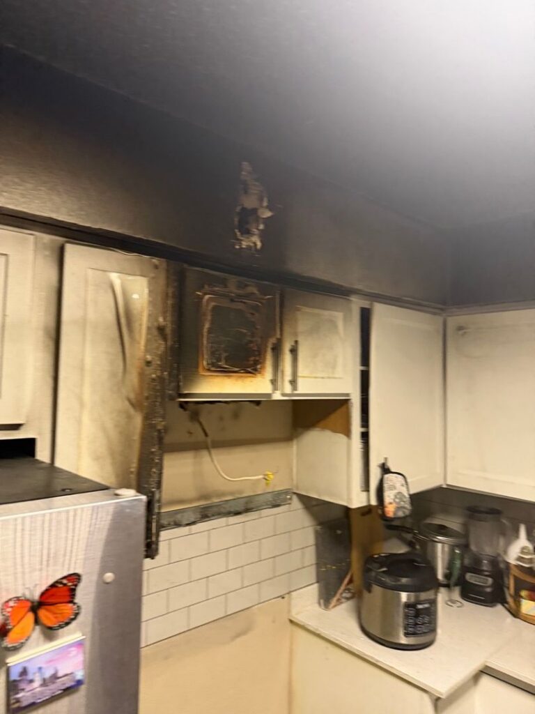 Extensive black soot and fire damage on kitchen cabinets and the ceiling above a countertop after a house fire.