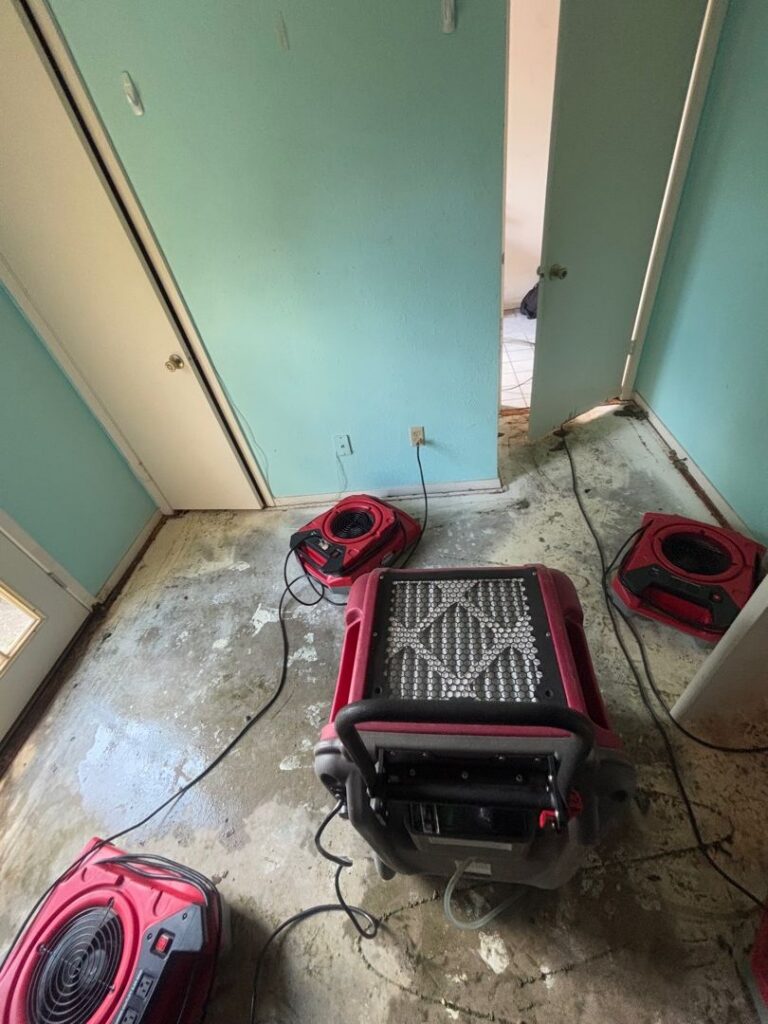 Commercial dehumidifier and air movers drying water damage caused by an appliance leak on concrete flooring.