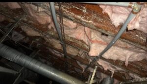 Crawl space with exposed insulation and pipes, illustrating conditions that promote mold growth in summer.