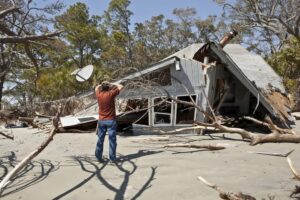 Distraught man surveys his hurricane-destroyed home and debris on a sandy coastline