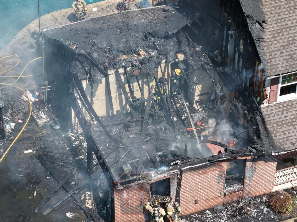 An aerial view shows firefighters working on a heavily charred house after a devastating fire. TITLE: