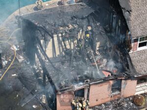 An aerial view shows firefighters working on a heavily charred house after a devastating fire. TITLE: