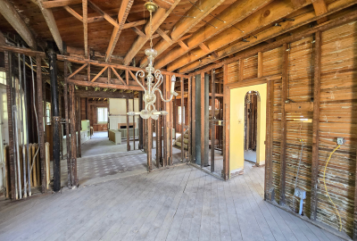 Exposed interior of a residential building during code-compliant reconstruction, showing open framing, ceiling joists, and stripped lath walls prepared for updated electrical and structural work.