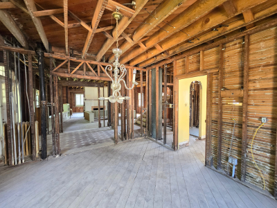 Exposed interior of a residential building during code-compliant reconstruction, showing open framing, ceiling joists, and stripped lath walls prepared for updated electrical and structural work.