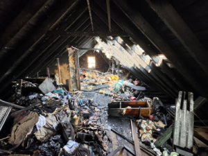 Severe attic destruction after a house fire showing smoke and debris before smoke damage restoration.