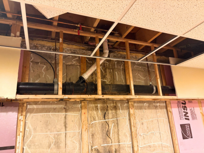 Open commercial wall section in Orland Park showing exposed pipes, damaged drywall, and wood framing in need of structural repair after water damage.