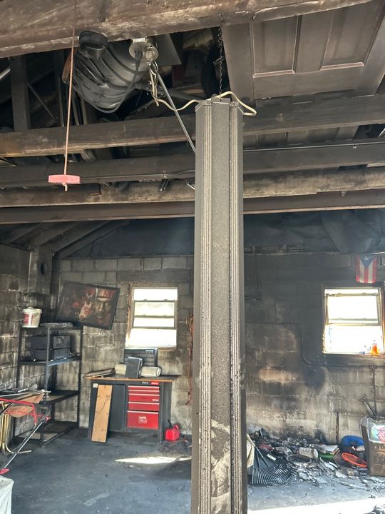 Thick soot and smoke damage covering a support beam, ceiling, and concrete block walls inside a garage after a fire.
