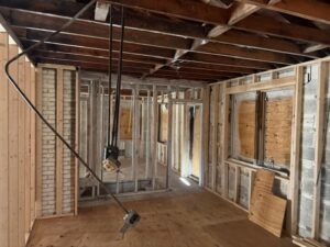 Interior view of a fire-damaged home undergoing reconstruction and repairs with exposed wall framing, electrical wiring, and structural restoration work.