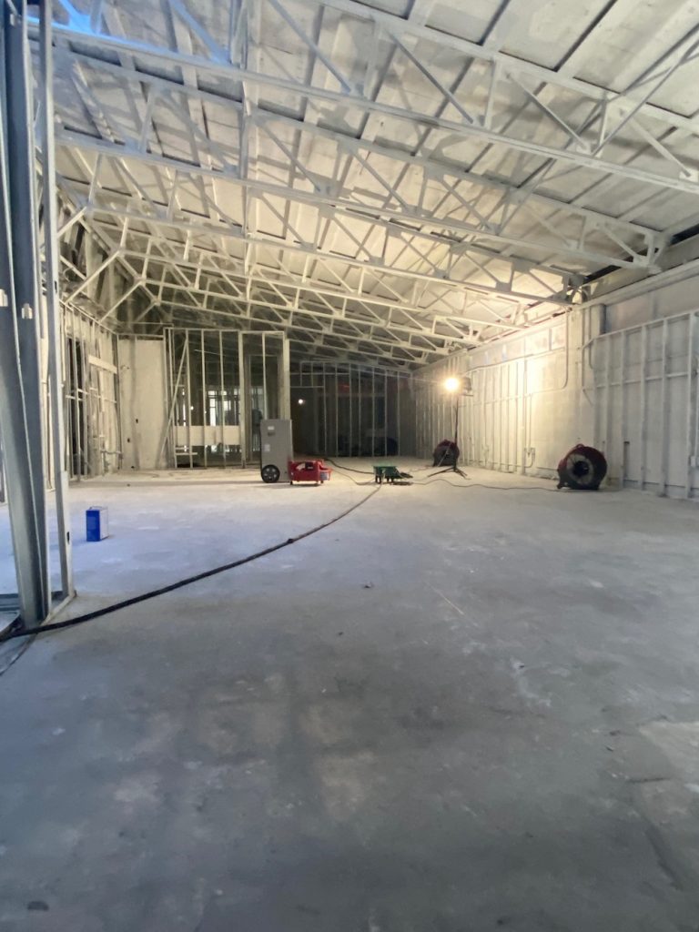 Interior view of a large building under construction with exposed metal framing and a concrete floor.