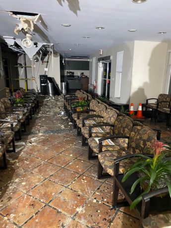 A damaged waiting room shows a partially collapsed ceiling with debris scattered across the tiled floor and patterned chairs