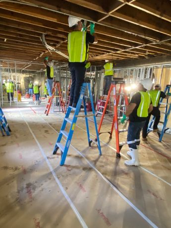Construction workers in hard hats and vests install ceiling components inside a building. TITLE