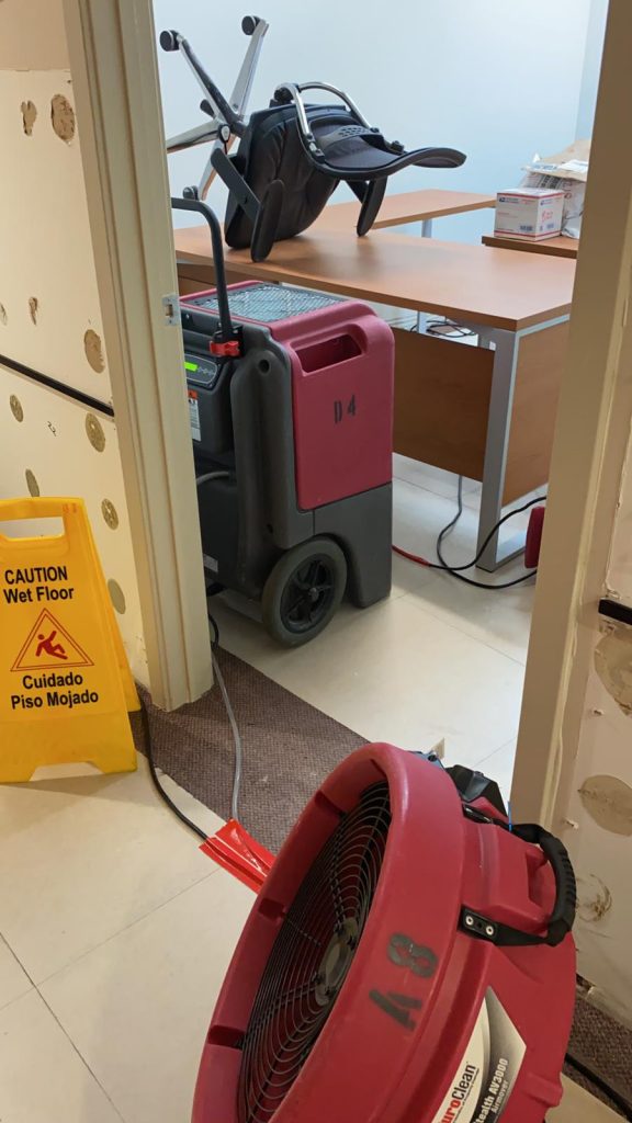 Water damage restoration equipment, including a dehumidifier and fan, is drying an office