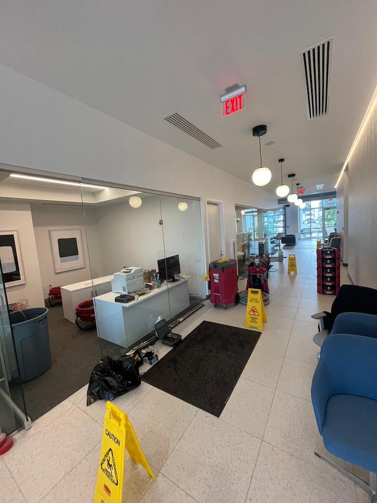 A modern office interior features a reception desk, hallway, and cleaning equipment with caution signs.