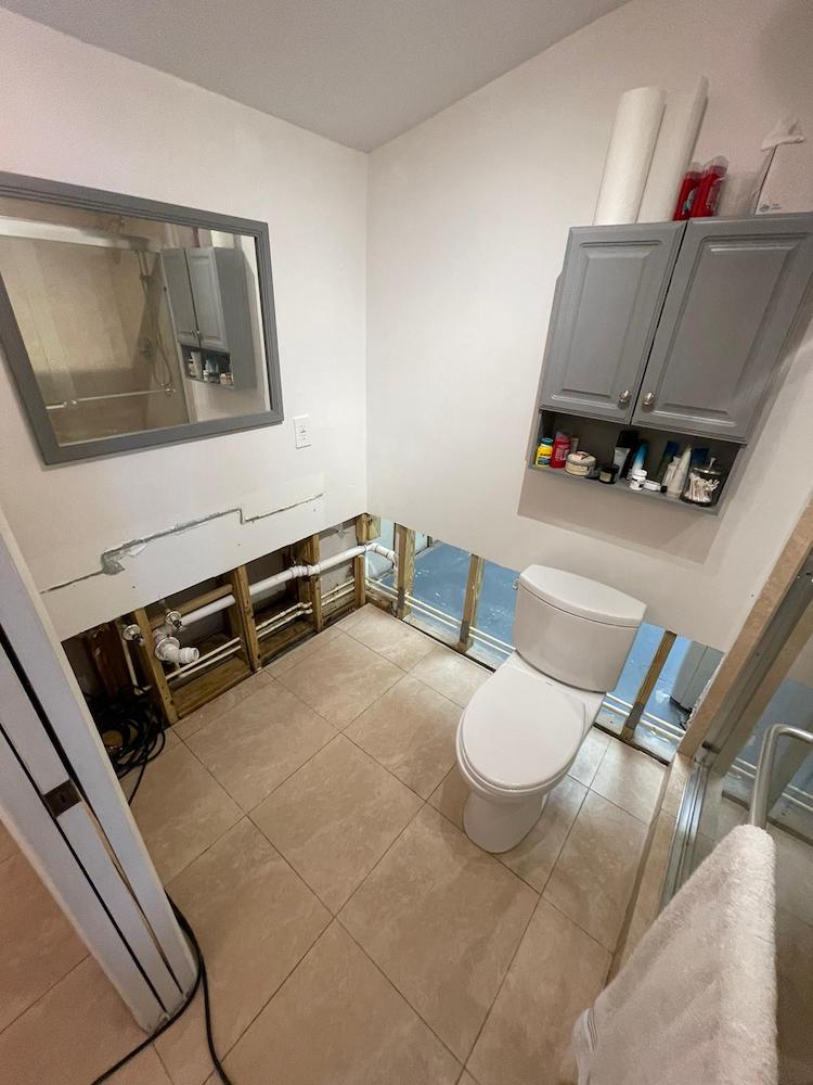 Bathroom under renovation with exposed wall studs, plumbing, and a toilet on a tiled floor.