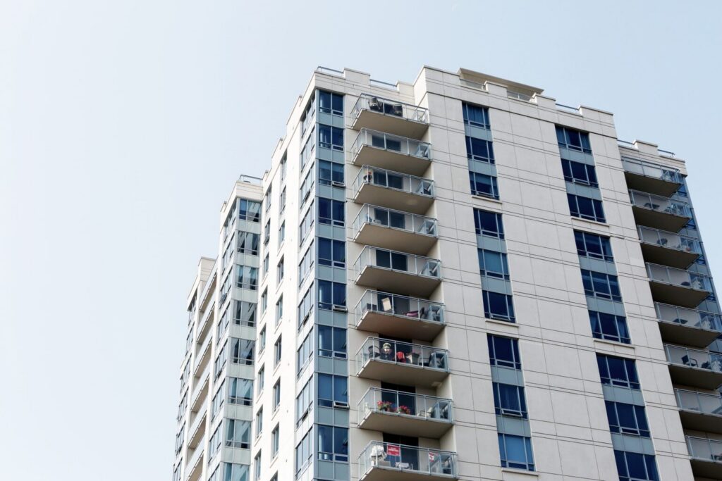 Tall residential building featuring multiple balconies and blue windows under a clear sky.