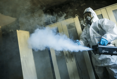 PuroClean fire restoration specialist using a thermal fogger to remove smoke odors in a living room