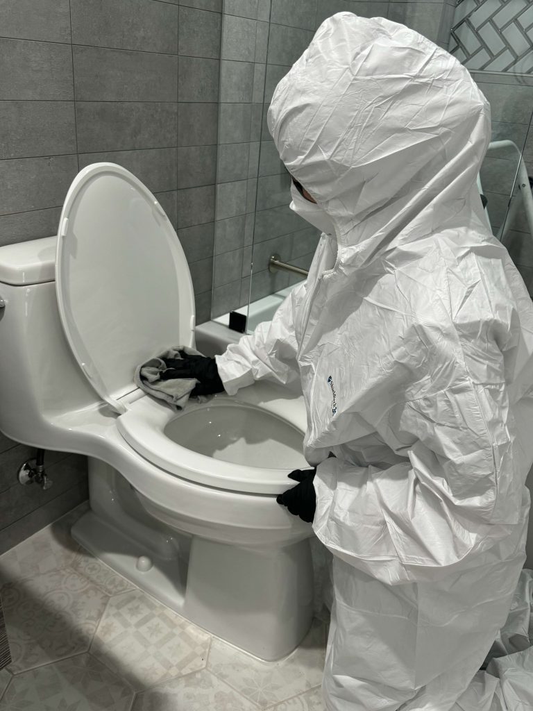 A person in a protective suit cleans a toilet in a modern bathroom.