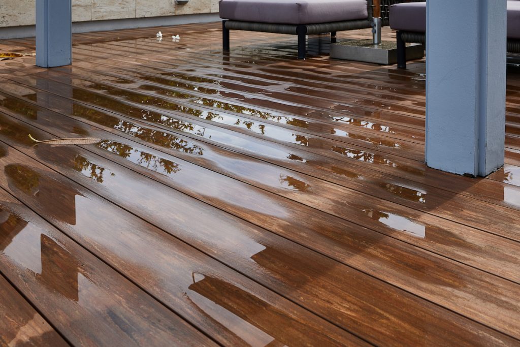 Wet hardwood floor with standing water, showcasing potential water damage on a deck area.