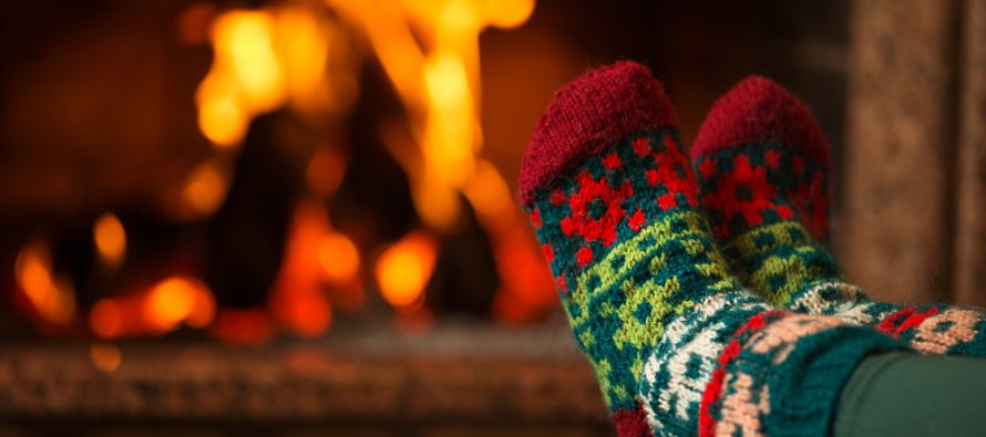 Cozy feet in colorful holiday socks resting near a warm fireplace.
