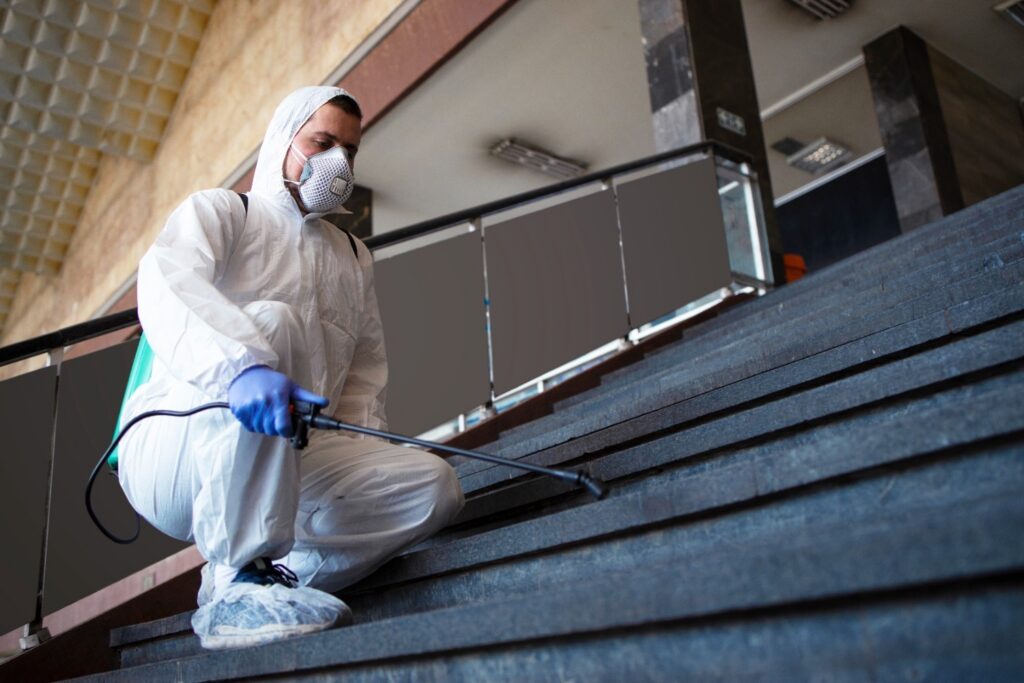 Person in white chemical protection suit disinfecting public corridors and steps to stop spreading highly contagious corona virus