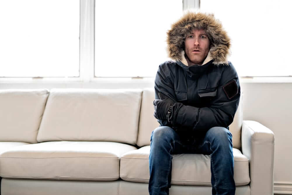 Man feeling cold indoors in winter jacket – learn how to prevent frozen pipes to keep your home warm