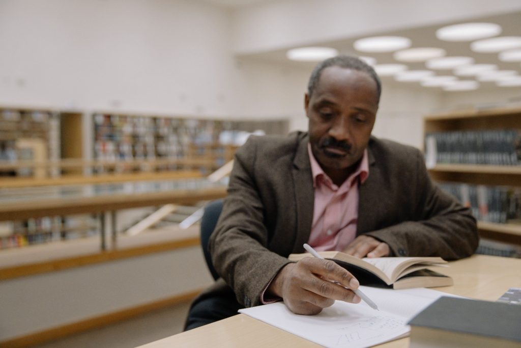 A man sitting inside the library while writing on the paper