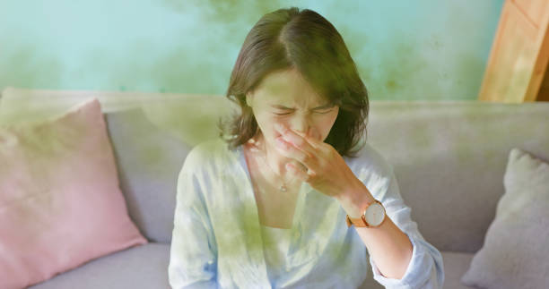 A woman pinches her nose with a disgusted expression as green gas surrounds her, indicating a bad