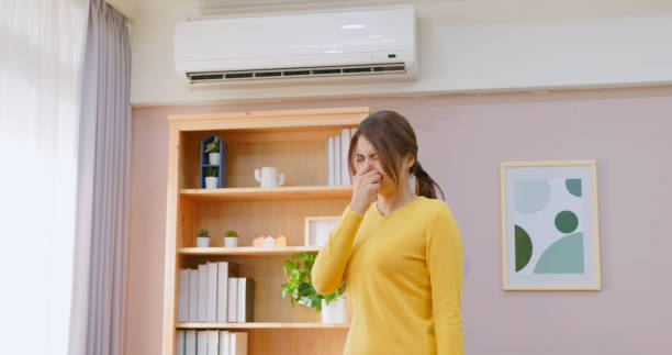 A woman pinches her nose in a room, bothered by a bad smell from the