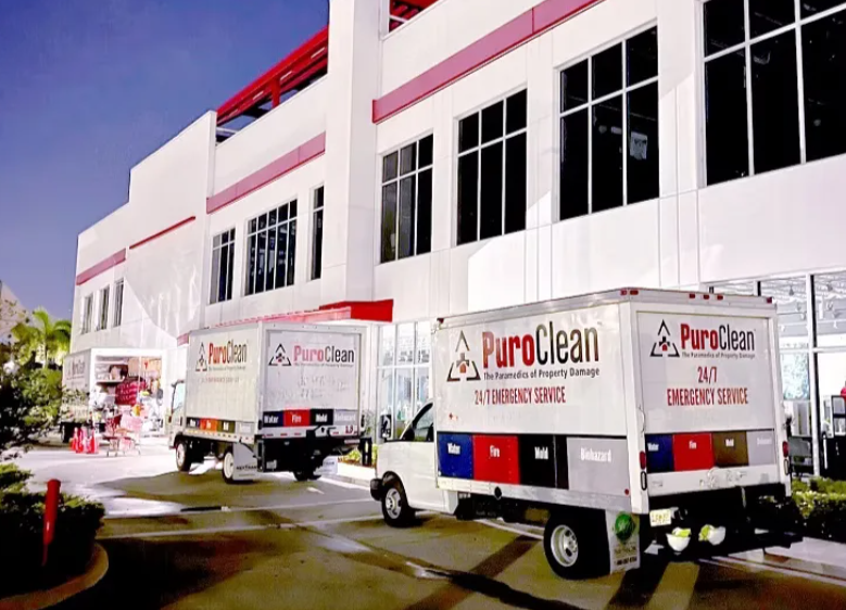 Two PuroClean emergency service trucks are parked at night outside a large commercial building. T