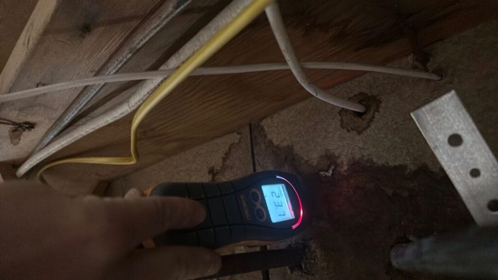 A moisture meter displays a high 23.7 reading on a water-stained wooden