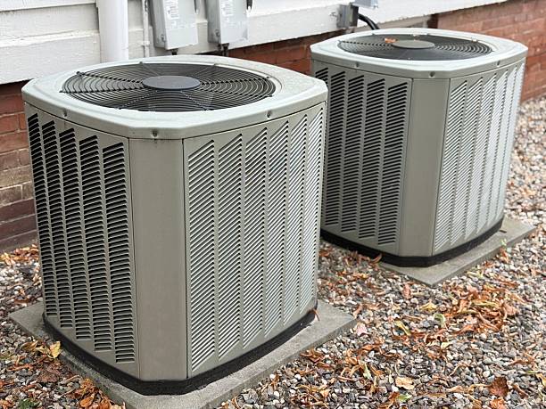 Two outdoor air conditioning units sit on concrete pads beside a house.