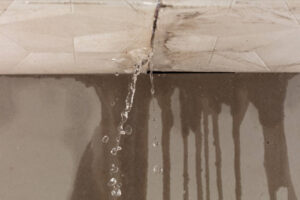 Clear water leaks from a ceiling crack, dripping onto a stained wall below.