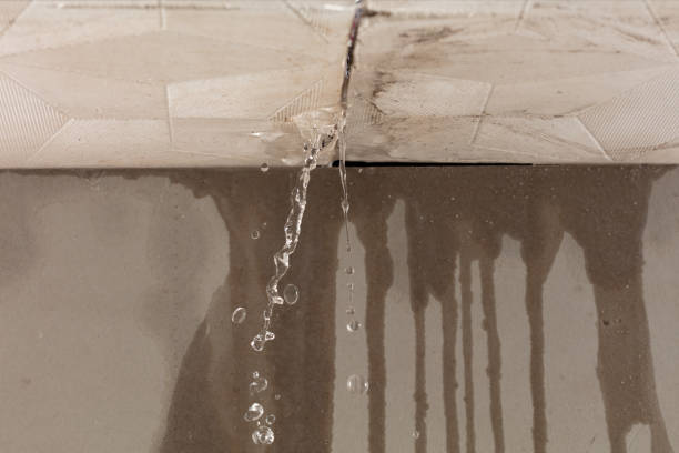 Clear water leaks from a ceiling crack, dripping onto a stained wall below.