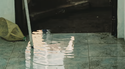 Standing water floods a tiled floor, reflecting light, with a pole and bottle